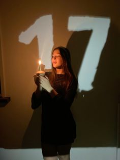 a woman holding a lit candle in front of a wall with the number seven drawn on it