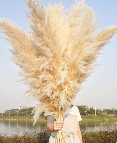 a woman holding a bunch of flowers in front of her face with the sky behind her