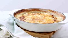 a casserole dish on a wooden board with a white towel and napkin next to it