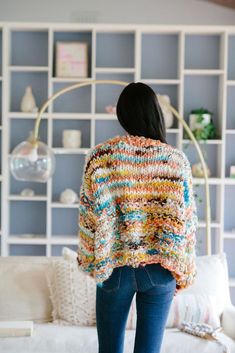 a woman standing in front of a couch wearing a multicolored knitted sweater