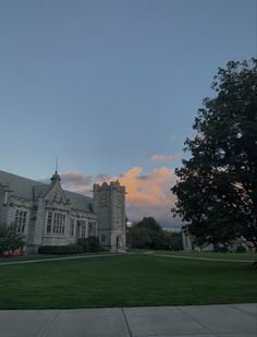 a large building with a tree in front of it on a grassy field at sunset