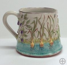 a ceramic mug with flowers and grass painted on the inside is sitting on a white surface