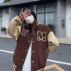 a man wearing a mask and jacket standing in front of a building with his hand up to his face