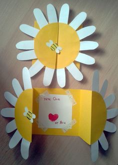 two sunflowers made out of paper on top of a wooden table next to each other