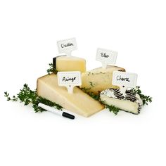 several different types of cheese are arranged on a white surface, with labels attached to them