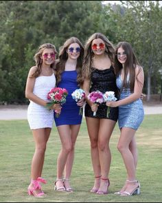 four young women in dresses and sunglasses posing for a photo on the grass with their bouquets