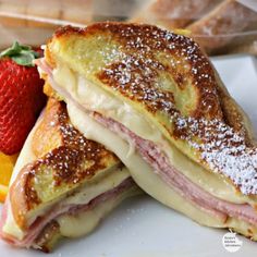 a sandwich with ham, cheese and strawberries on a plate next to some fruit