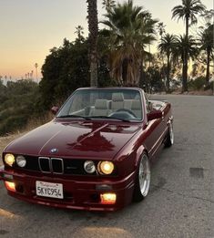 a red car parked on the side of a road next to trees and palm trees