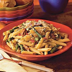 a plate full of pasta and vegetables on a wooden table with bread in the background