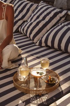 a woman sitting on top of a bed next to a tray filled with drinks