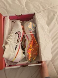 a person is holding a pair of nike shoes in a pink box on a bed