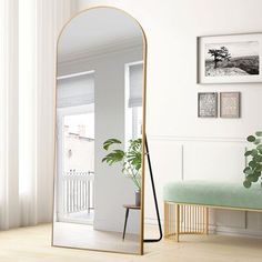 a large mirror sitting on top of a wooden floor next to a green bench and potted plant