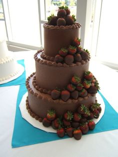 a three tiered chocolate cake with strawberries on the top and bottom, sitting on a blue table cloth