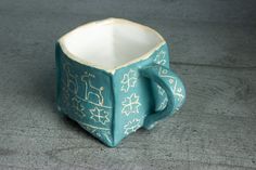 a teal ceramic cup with white designs on the outside and inside, sitting on a gray surface