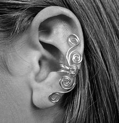 a woman's ear is adorned with silver wire and has an intricate design on it