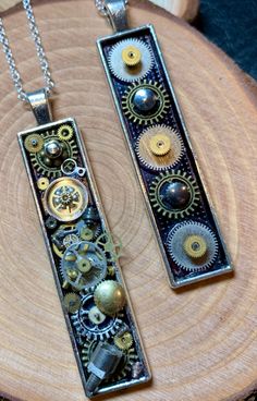 two necklaces with gears on them sitting on top of a piece of wood