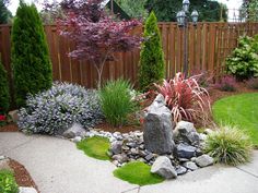 a small garden with rocks and plants in the center, along side a wooden fence