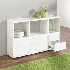 a white bookcase with drawers and plates on top in a room that has green rugs