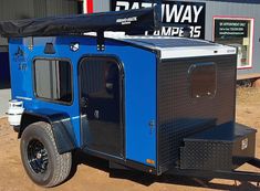 a small blue trailer parked in front of a building with a black cover on it