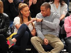 a man and woman sitting next to each other in front of a crowd at a basketball game