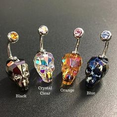 four different colored jeweled skull belly piercings on a black surface with the words crystal clear, orange, and blue written below them