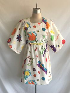 "One-of-a-kind, handmade novelty cotton mini dress made from a 1970's Butterick pattern! Dress features kimono sleeves, square neck, A line silhouette in a vintage Hawaiian print with kids drawings and writing. A hand crocheted piece of yellow cotton lace decorates the front waist seam. Waistline is between an empire and a natural waist. Dress is lined in the bodice and zips up the back with a plastic teeth zipper.  Never worn, made specially for Kinfauns!  Fabric designed and printed in Hawaii Vintage Cotton Mini Dress, Vintage Cotton Mini Dress With Square Neck, Multicolor Square Neck Cotton Dress, Multicolor Cotton Dress With Square Neck, Multicolor Cotton Mini Dress For Daywear, Multicolor Cotton Square Neck Dress, Vintage Cotton Mini Dress For Summer, Vintage Cotton Mini Dress For Spring, White Vintage Mini Dress With Square Neck