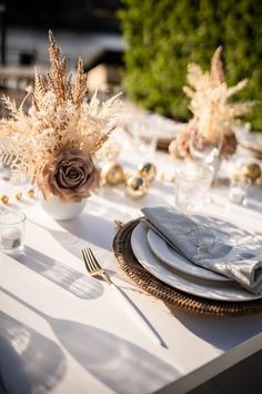 the table is set with white and gold plates, silverware, and flower centerpieces