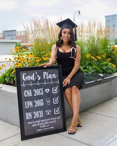 a woman in graduation cap and gown sitting next to a sign