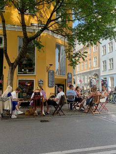 people sitting at tables in front of a yellow building on the side of a street