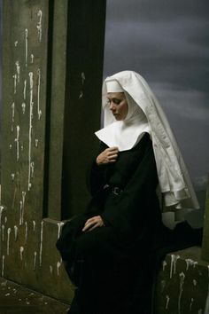 a nun is sitting on the floor with her hands in her pockets and looking down