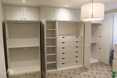 an empty walk in closet with white cabinets and drawers on the floor, next to a lamp