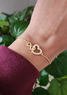 "This 18K gold bracelet is made with gold a linked heart & infinity on a gold adjustable chain. Heart & infinity measures approximately 1\" x .5\" (heart).  The gold brass chain has a ball and joint closure that slides to adjust to the size you need. It can fit almost any size wrist. Slide the ball to the end in order to slide the bracelet over your hand onto your wrist. Slide the ball to tighten it to the size you desire. The remaining chain dangles with 2 small crystals at the ends. This fits most wrist sizes (5-9\")." Heart-shaped Adjustable Chain Bracelet For Anniversary, Heart-shaped Anniversary Bracelet With Adjustable Chain, Adjustable Heart-shaped Gold Jewelry, Infinity Heart Bracelet For Anniversary, Elegant Infinity Heart Bracelet As Gift, Elegant Infinity Heart Bracelet For Gift, Elegant Infinity Heart Bracelet Gift, Adjustable Gold Infinity Chain Bracelet, Adjustable Double Heart Chain Bracelet Gift