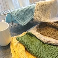 several knitted blankets on a table next to a coffee cup