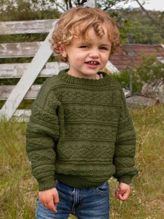 a little boy standing in the grass with his hands in his pockets and smiling at the camera