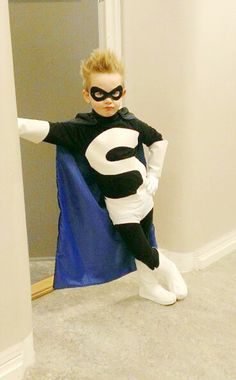 a young boy dressed up as a catwoman in a room with a blue cape and white shoes