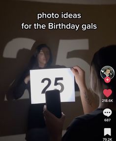 a woman is holding up a sign with the number twenty five on it and she is looking at her phone