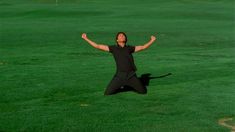 a man jumping in the air with his arms wide open on a green grass covered field