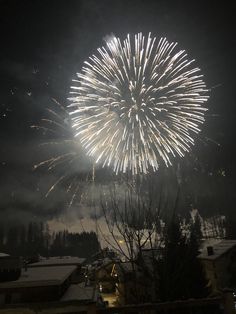 fireworks are lit up in the night sky above snow - covered houses and trees,