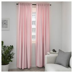 a living room with pink curtains and a white couch in front of a window that has potted plants on it