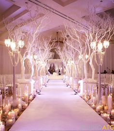 the aisle is lined with candles and decorated with white trees for an elegant winter wedding