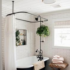 a bathroom with a black and white bathtub next to a window filled with potted plants