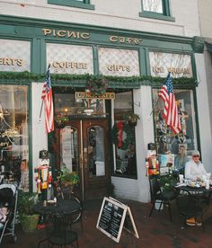 people are sitting at tables in front of a coffee shop with american flags hanging from the windows