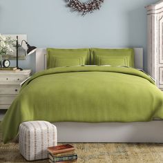 a bed with green sheets and pillows in a bedroom next to a white chest of drawers