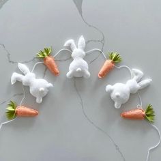 four white stuffed rabbits with carrots attached to wires on a table top, in the shape of bunnies