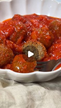 a white bowl filled with meatballs covered in marinara sauce next to a fork