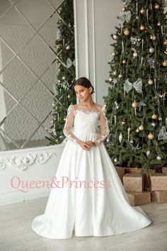 a woman standing in front of a christmas tree wearing a wedding dress with long sleeves