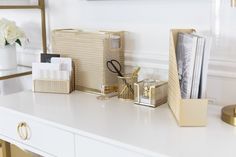 a white desk topped with boxes and other items next to a vase filled with flowers