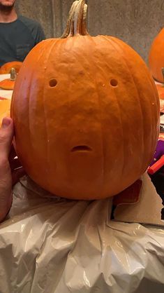 a person holding up a giant pumpkin in front of their face and another man behind them