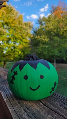 a green pumpkin sitting on top of a wooden table in front of some trees and blue sky