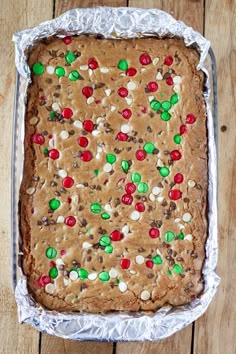 a cookie cake with candy and m & m on it sitting in a tin foil pan